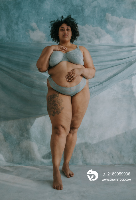 full body portrait of a plus size afro indigenous person standing with hand on chest and hand on bel