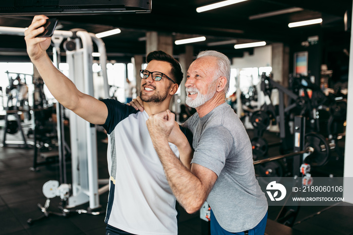 .Senior man taking selfie photo with his personal trainer while exercising at gym.