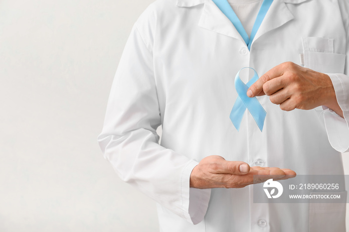 Male doctor with blue ribbon on light background. Prostate cancer awareness concept