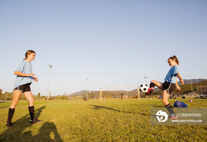 Side view of players practicing soccer on grassy field against clear sky