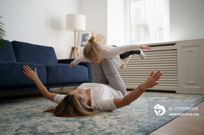 Young mother with little daughter practicing yoga at home. Family fizical activity, sporty mom and k