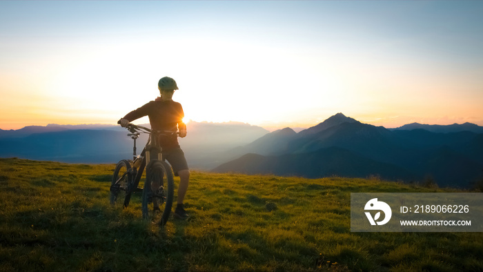 Woman walking uphill with mountain bike at a sunset.