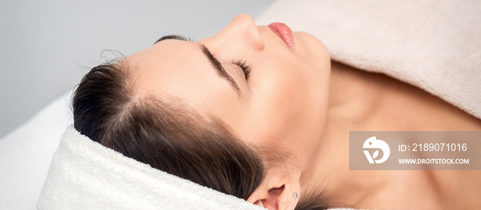 Side view of young woman lying on beautician table with closed eyes while waiting for cosmetic proce