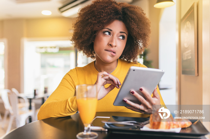 Young afro woman having a breakfast at cafe. She is drinking an orange juice and eating and a croiss