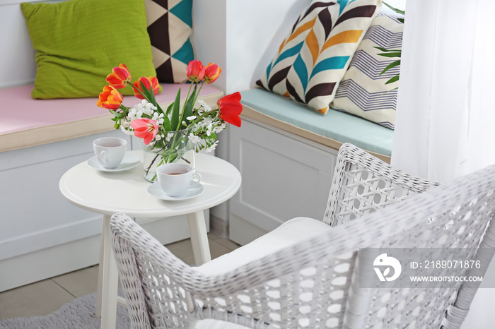 Vase with beautiful flowers and tea set on table in modern veranda interior