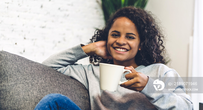 Portrait of smiling happy african american black woman relaxing drinking and looking at cup of hot c