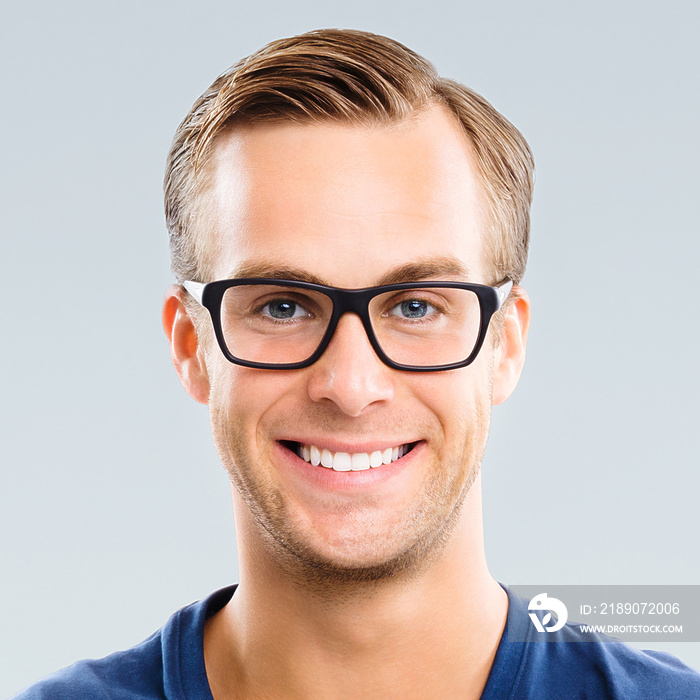 灰色背景下，一个戴着眼镜、面带微笑的年轻人的肖像。白人男性