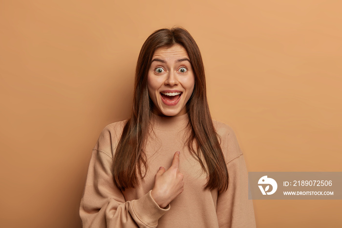 Who, me? Portrait of beautiful surprised woman points at herself and looks with happy amazed express