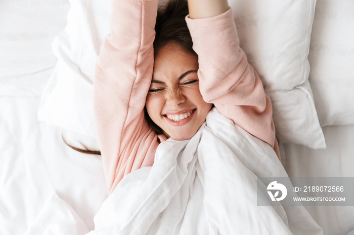 Cheerful lovely young girl wearing pajamas laying in bed