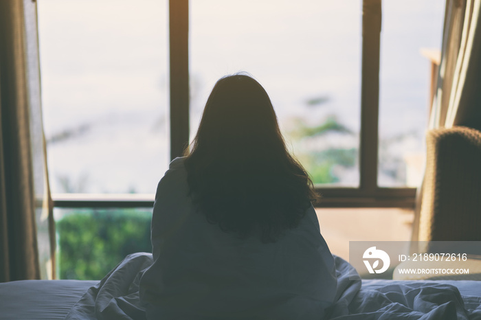 A woman sitting in the bed looking at beautiful sea view through the window after waking up in the m