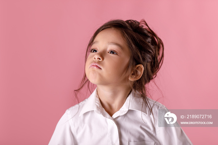 Cute proud little girl in white shirt on pink background. Human emotions and facial expression