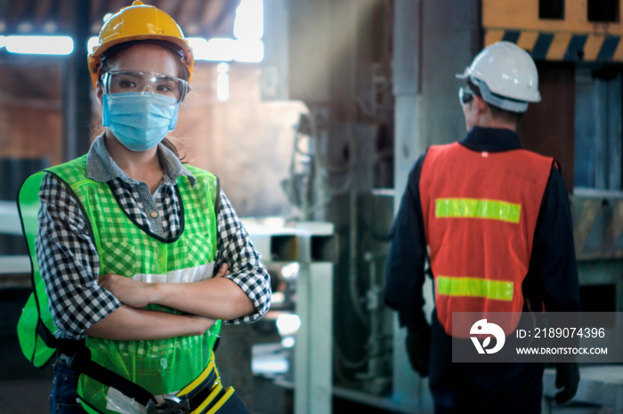 Industrial engineer worker wearing helmet, safe glasses and mask with arms crossed at manufacturing 