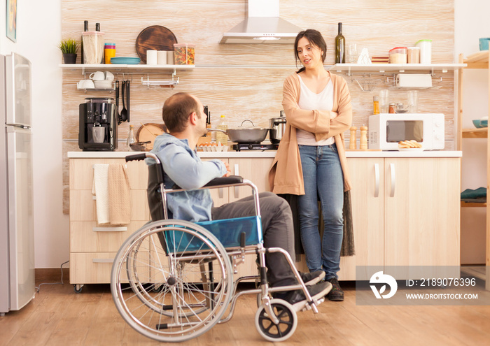 Disabled man in wheelchair spending time with wife in kitchen. Disabled paralyzed handicapped man wi