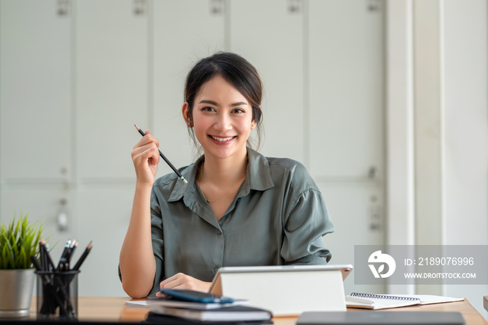 一位面带微笑的美丽亚洲女商人正拿着铅笔看着镜头。