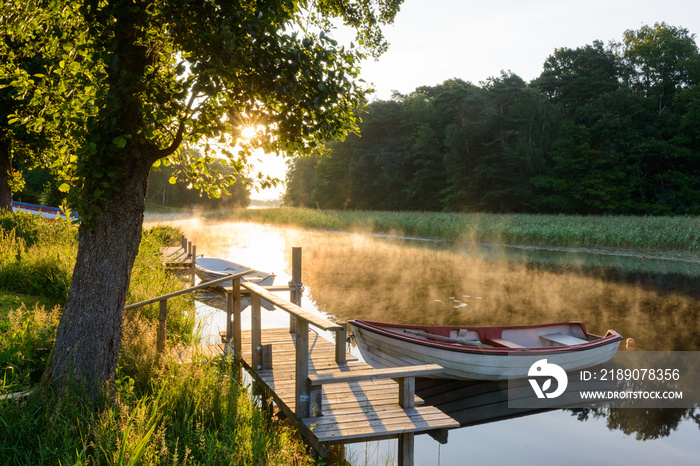 Rowboats moored on a sunlit and misty lake. Sweden