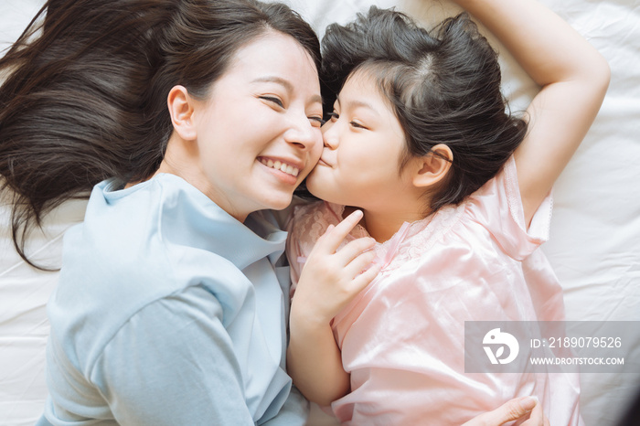 Daughter kisses her mothers cheek. and hugging in the bedroom .Happy Asian family