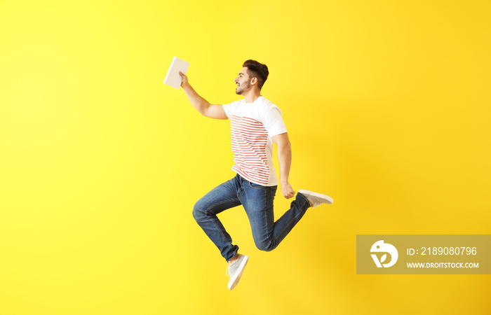 Jumping young man with book on color background