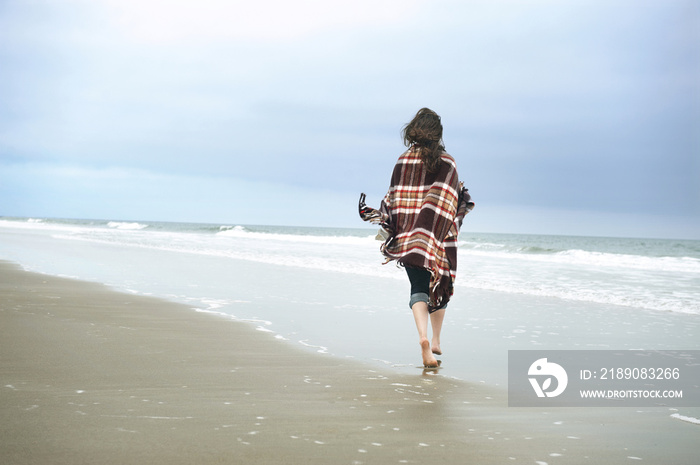 裹着毯子走在海边的女人的后视图