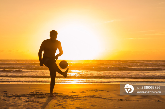 Great concept of soccer, man playing soccer on the beach in golden hour, sunset. Making keepie uppie