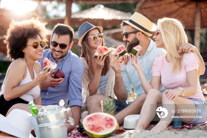 Happy young friends eating watermelon on beach