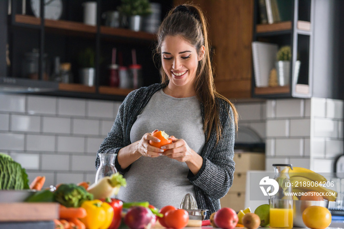 Beautiful smiling young pregnant woman preparing healthy food with lots of fruit and vegetables at h