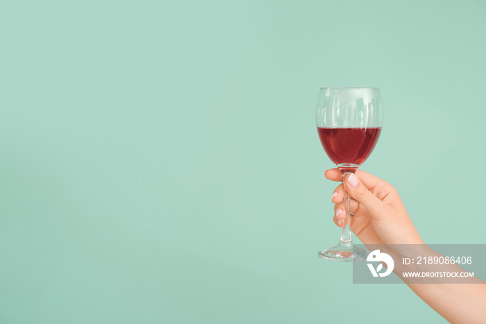 Hand with glass of wine on color background