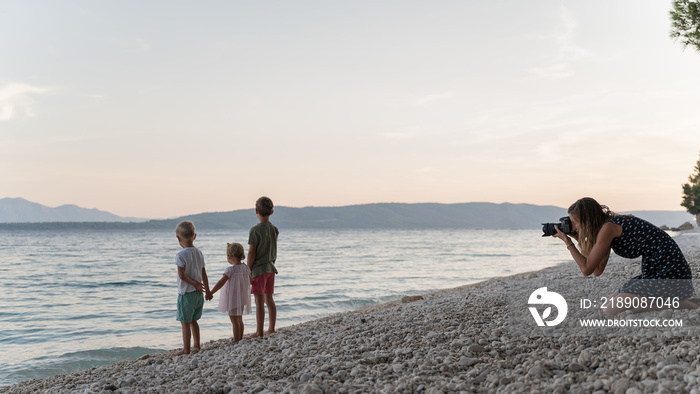 Young mother taking photos of her three kids at the beach