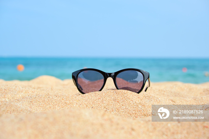 阳光明媚的热带海边沙滩上黑色防护太阳镜的特写。夏天