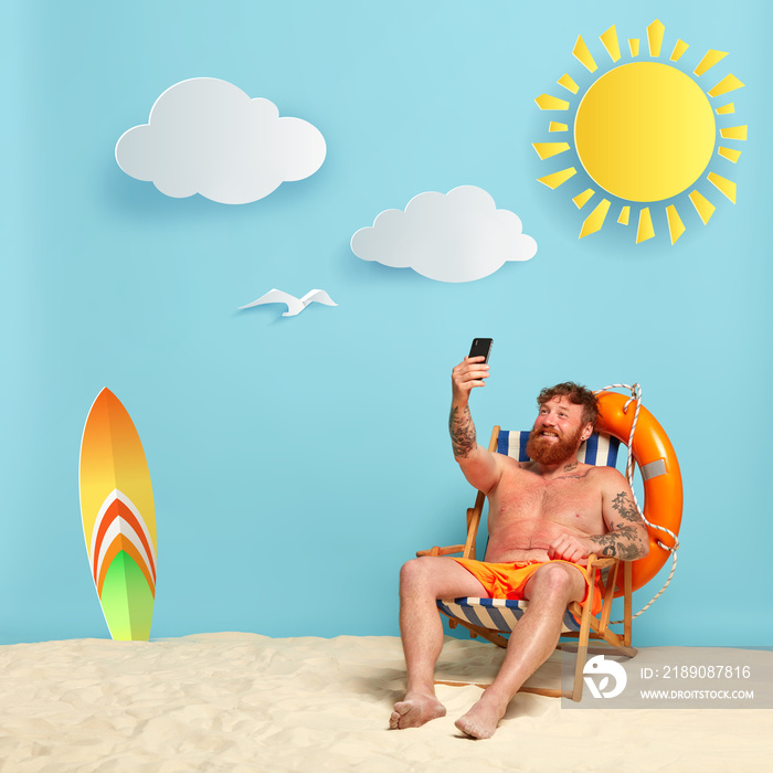 Happy shirtless ginger man makes selfie on beach chair, shares pics with friends online, rests in pa