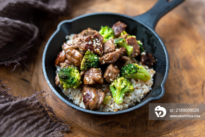 Beef and broccoli over rice in a black skillet topped with sesame seeds 