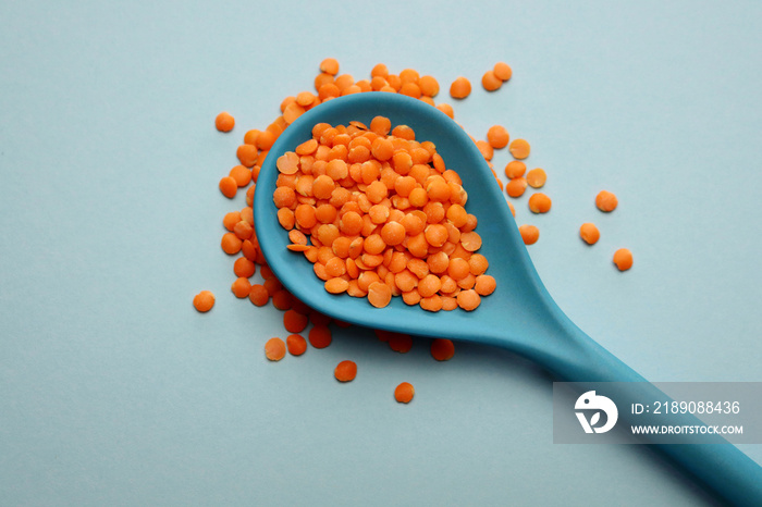 Red lentils in a blue bamboo spoon on a light blue background.