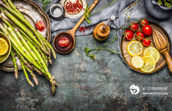 Tasty asparagus cooking with tomatoes, lemon and seasoning, preparation on rustic kitchen table with