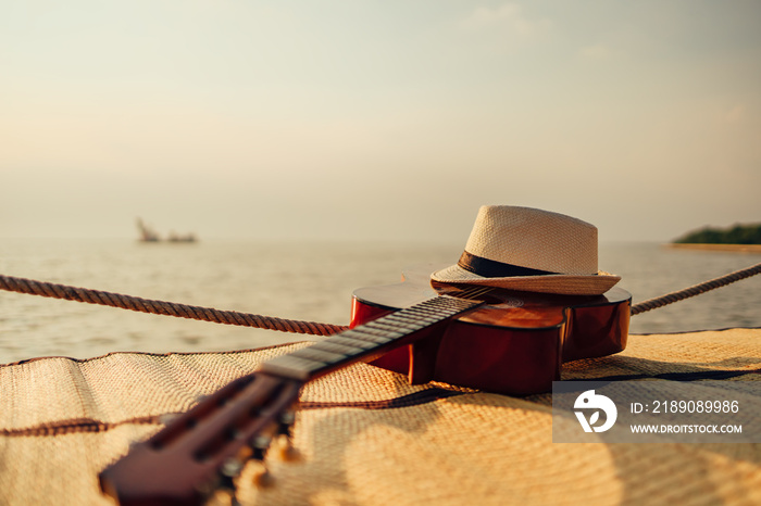 Guitar and hat on reed mat near the sea at sunset. Travel, vocation, holiday, summer concept.