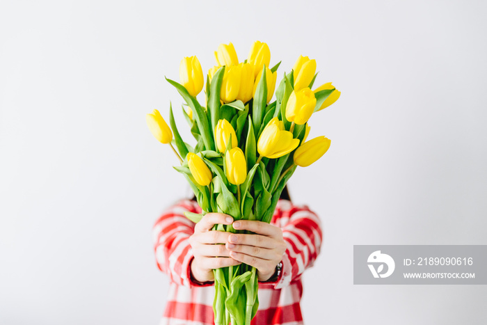 女人拿着一束黄色郁金香。用鲜花遮住脸。春天的浪漫概念