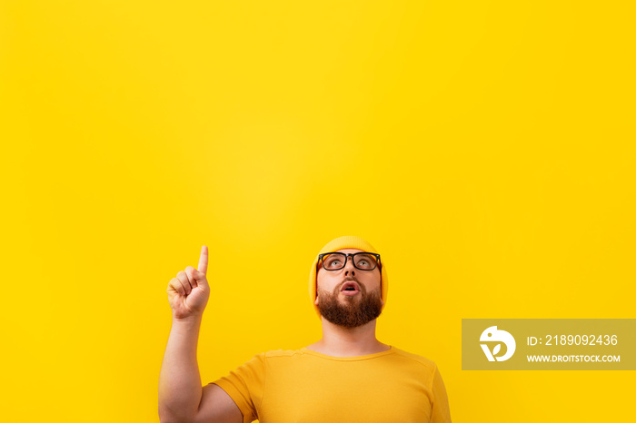 surprised bearded man with finger up, looking up over yellow background, advertising concept