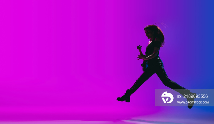 Silhouette of young female guitarist isolated on gradient background in neon.