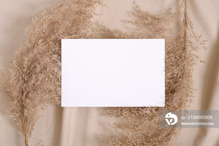 White blank paper card mockup with pampas dry grass on a beige neutral colored textile