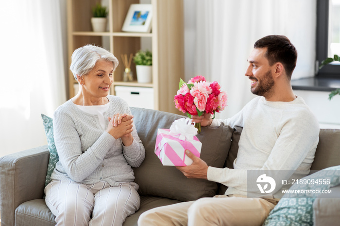 family, mothers day and birthday concept - smiling adult son giving present and flowers to his seni