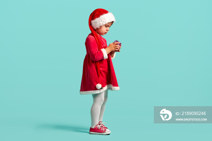 Adorable small baby girl in christmas hat and red dress on the studio background