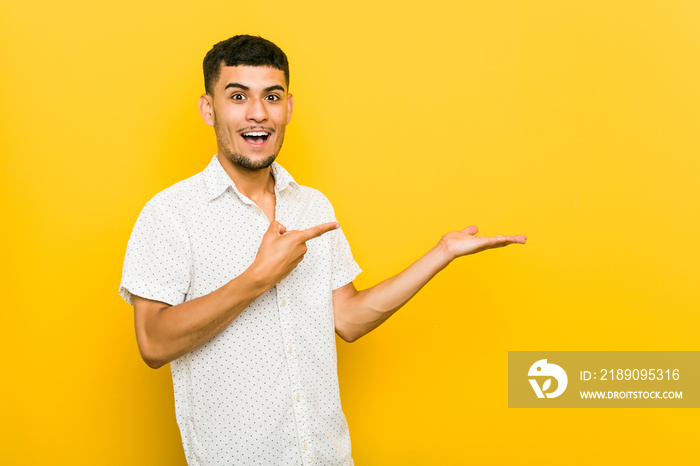 Young hispanic man excited holding a copy space on palm.