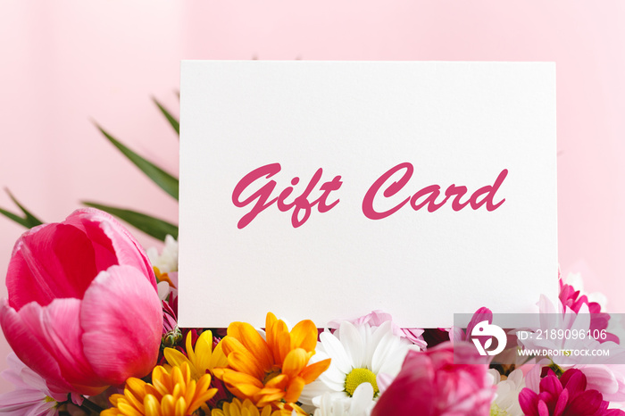 Gift card in flowers bouquet on pink background. Gift card present coupon for woman. Surprise vouche