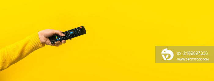 remote control in hand over yellow background, panoramic mock-up with space for text