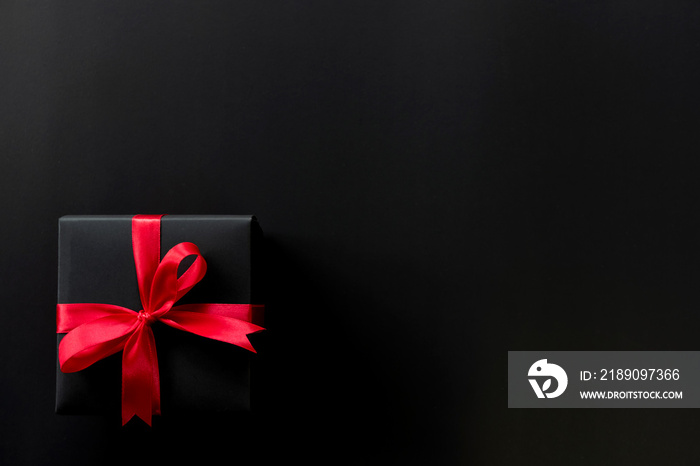黑色圣诞礼盒的俯视图，黑色背景上有红丝带，文本有复制空间。