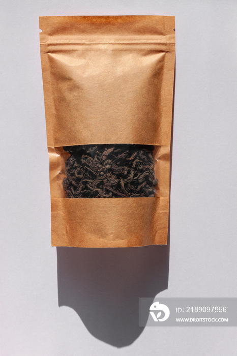 Brown kraft paper pouch bags with black tea leaves top view with harsh shadow on white background. P