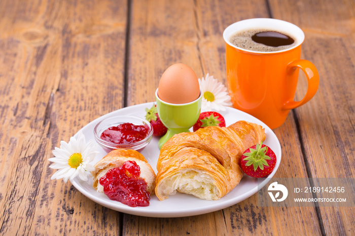 Delicious breakfast with croissant, fruits, boiled egg and  cup of coffee on wooden table