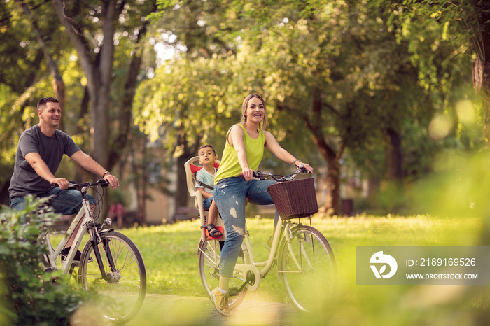 微笑的爸爸妈妈带着孩子骑着自行车在公园里玩。