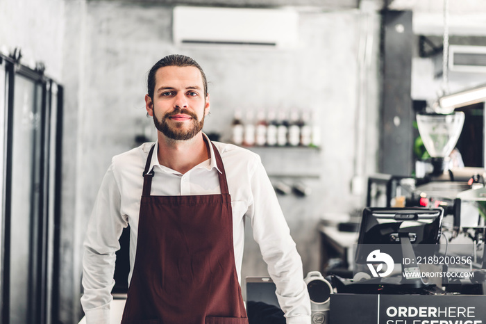 Portrait of handsome bearded barista man small business owner smiling behind the counter bar in a ca