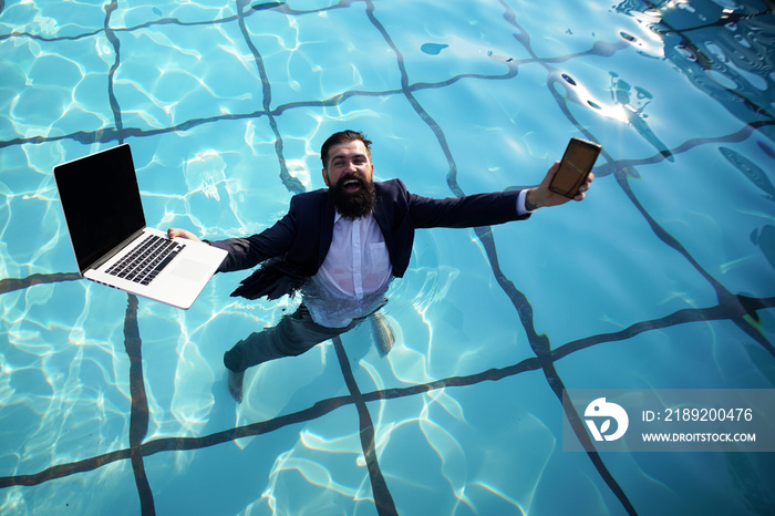 Crazy comic business. Funny businessman in suit with laptop and mobile phone on swimming pool.