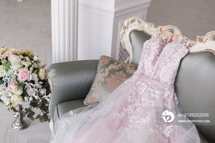 Luxurious pink wedding dress is lying on a grey sofa in a white room