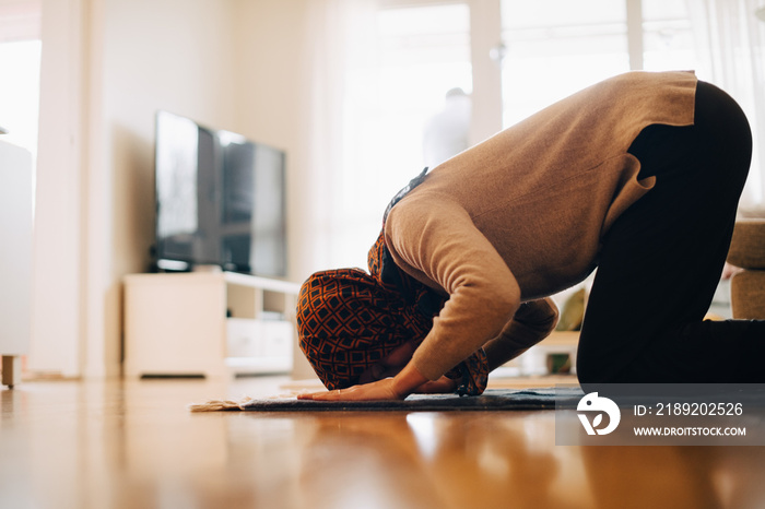 Mature woman praying on carpet at home